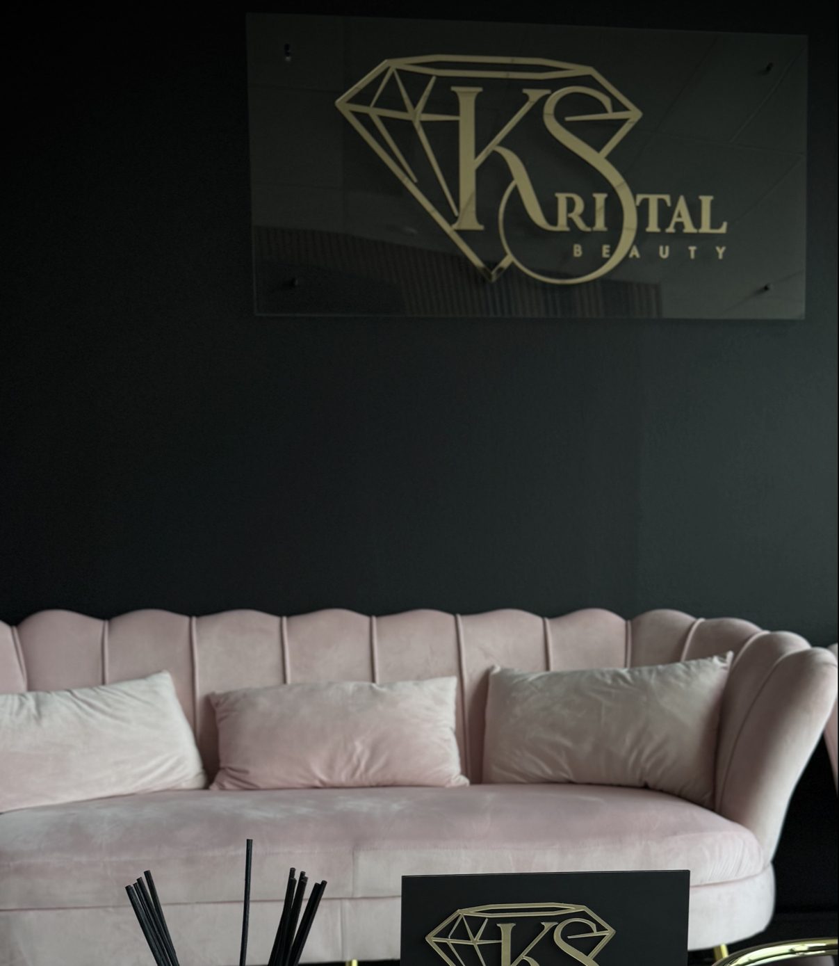 De salon van Kristal Beauty: gouden Kristal Beauty-sign op een donkergroene wand boven een roze velours schelpsofa