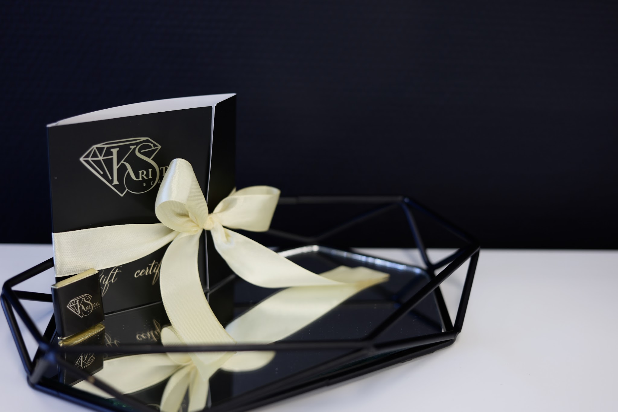 Een zwarte Kristal Beauty-geschenkdoos met crèmekleurig lint op een geometrisch dienblad
